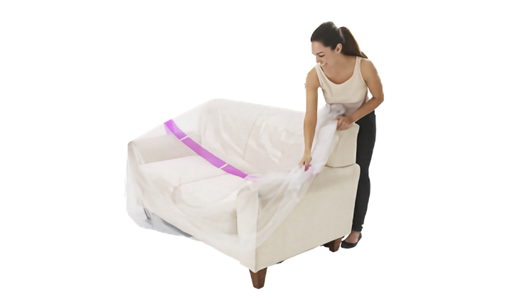 A woman is shown wrapping a clear plastic protective couch cover with a pink stripe around a cream-colored armchair against a solid white background.