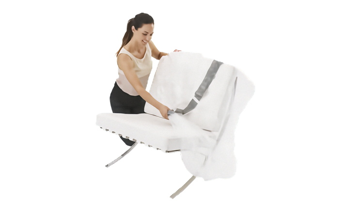 A woman in a white tank top and black skirt is shown from the side, fastening a clear plastic lounge chair cover onto a white lounge chair with a chrome metal frame, isolated on a white background.