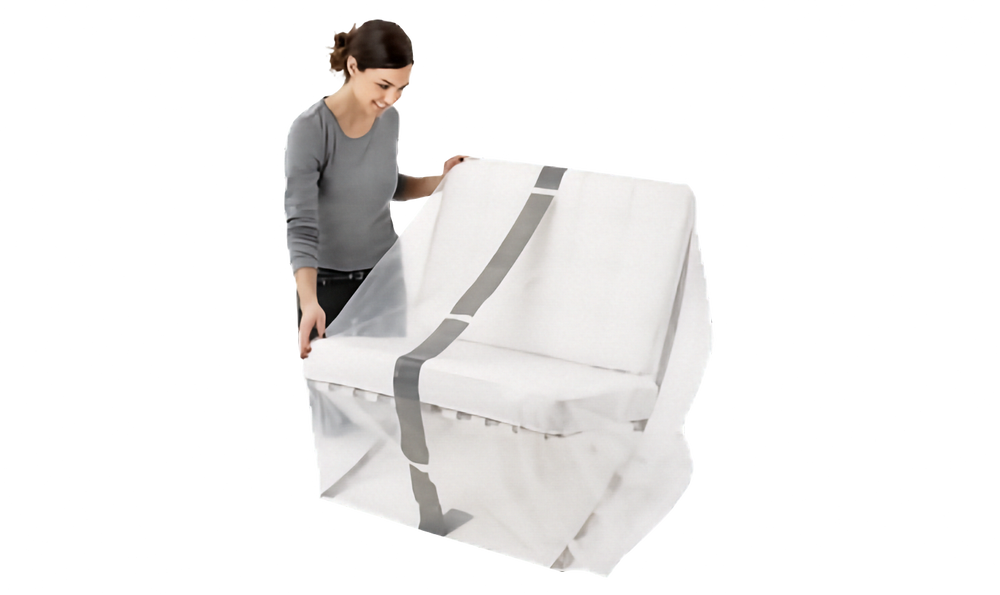 A woman in a gray long-sleeve top and black pants is holding a clear protective lounge cover with gray stripe over a chair, shown against a plain white background.