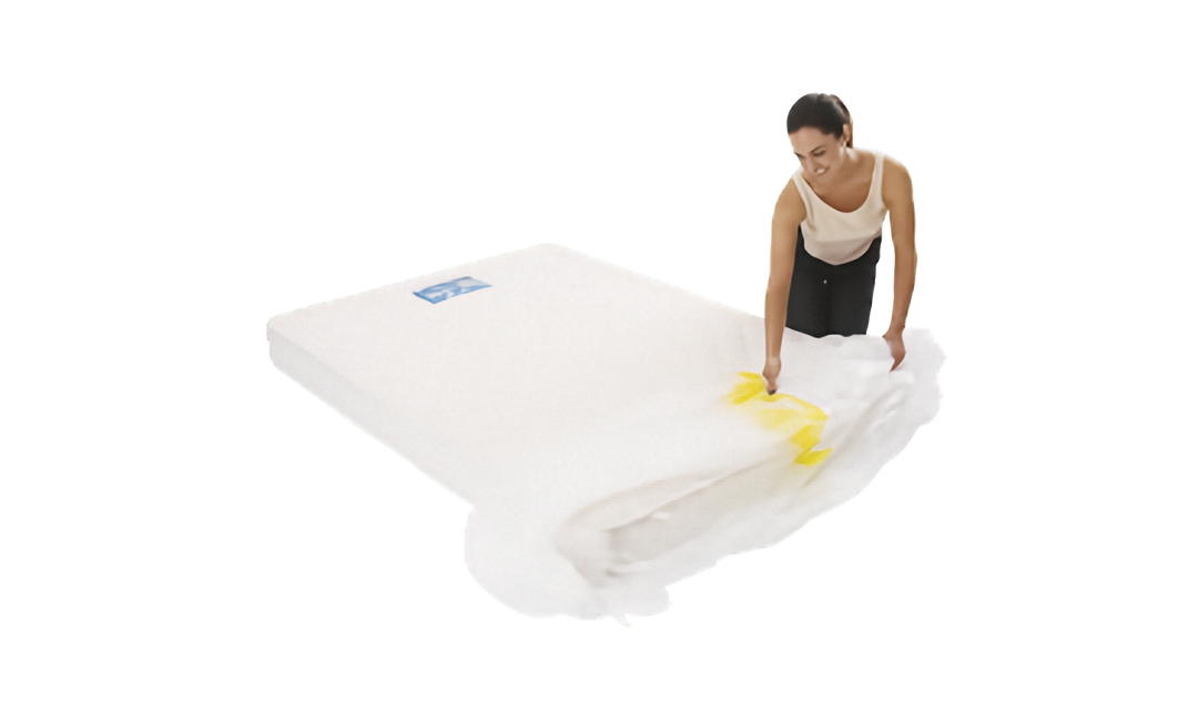 A person is shown sliding a clear plastic mattress protector onto a mattress. The cover has a yellow strip. Shown on a plain white background.