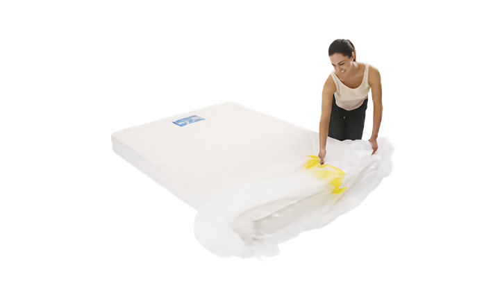 A person is shown sliding a clear plastic mattress protector onto a mattress. The cover has a yellow strip. Shown on a plain white background.