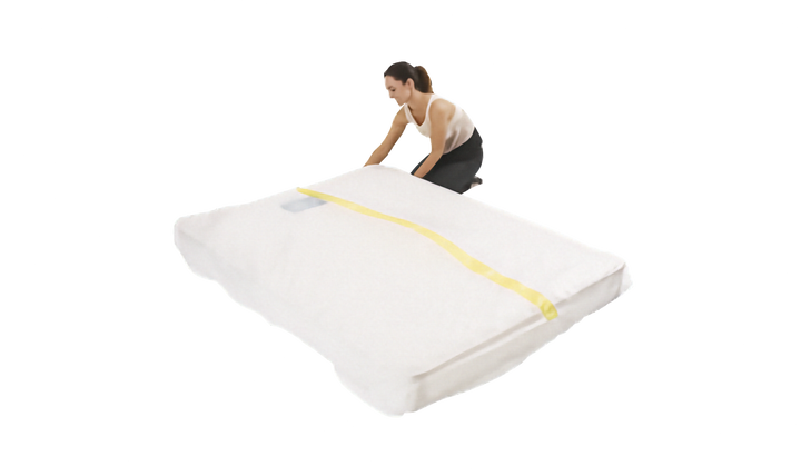 A person is shown sliding a clear plastic mattress protector onto a mattress. The cover has a yellow strip. Shown on a plain white background.