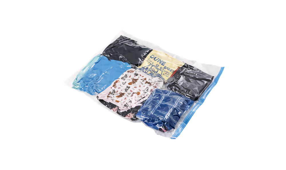 A clear plastic vacuum sealer zip-top bag with a blue zipper, shown on a white background. Inside, several folded garments are visible, including a bright blue item, a black garment, a cream/yellow garment with blue text, a white patterned garment, and a dark blue garment.