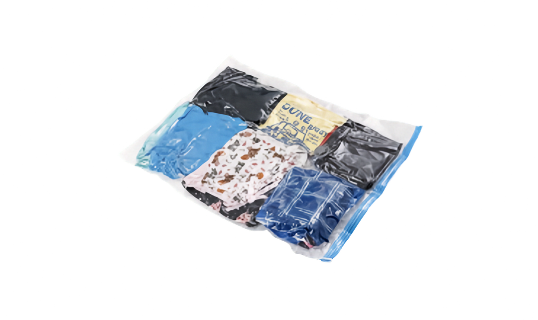 A clear plastic vacuum sealer zip-top bag with a blue zipper, shown on a white background. Inside, several folded garments are visible, including a bright blue item, a black garment, a cream/yellow garment with blue text, a white patterned garment, and a dark blue garment.